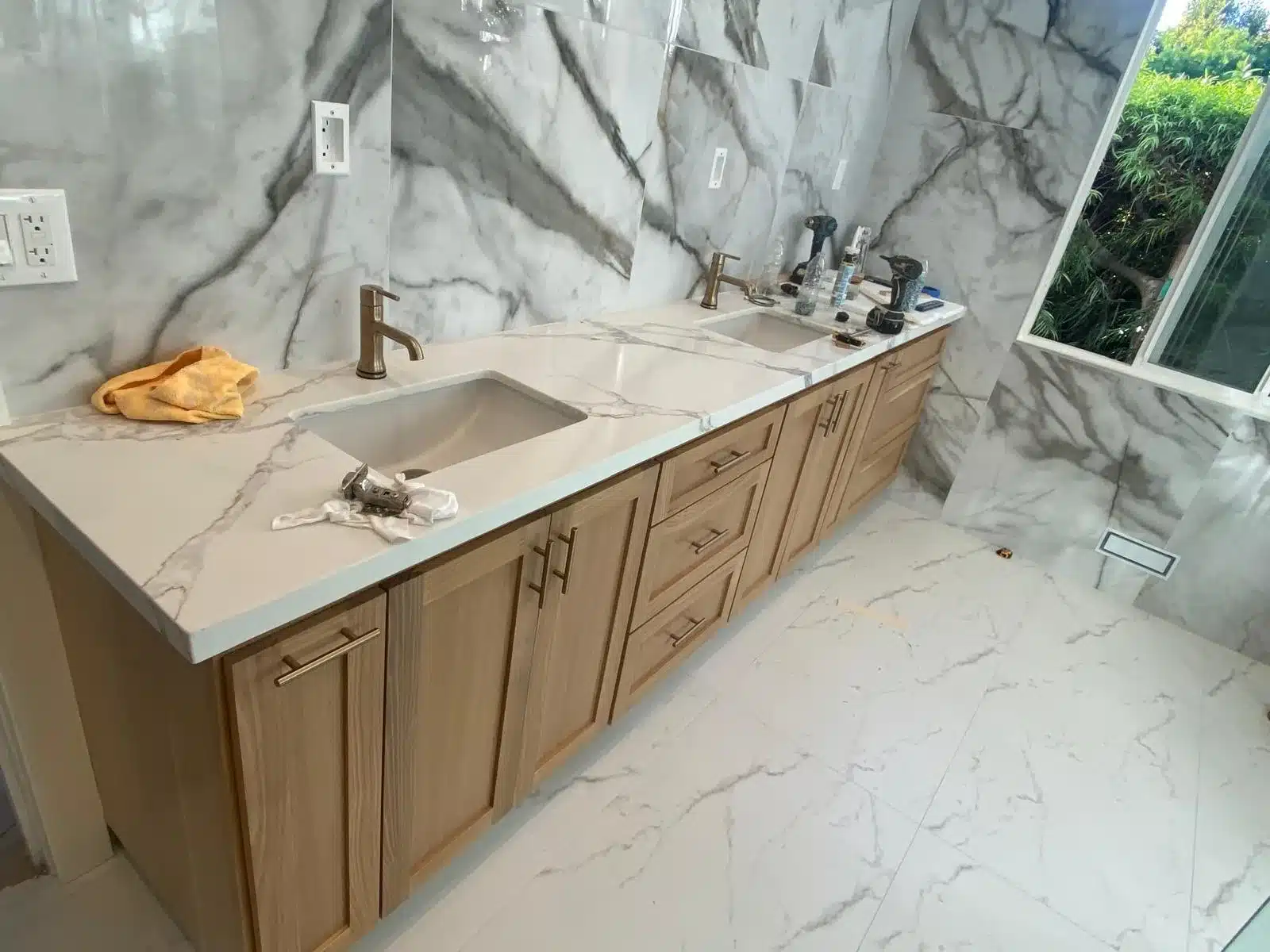 Long wood double vanity with undermount sinks, bronze-tone faucets, and gray-veined walls and countertop.