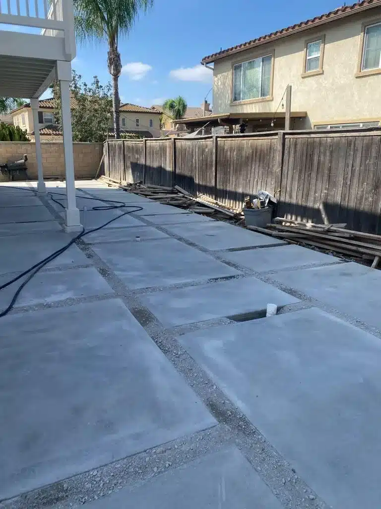 Backyard concrete grid with gravel-filled joints, not synthetic turf, beside a white pergola and wooden fence.