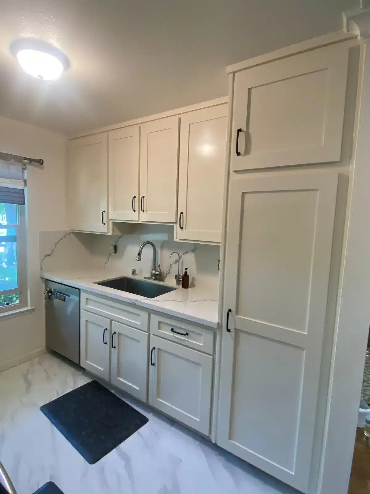 White cabinets with black pulls, a gray-veined counter and backsplash, an undermount sink, and a stainless dishwasher.