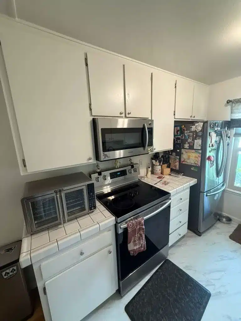 White flat-panel cabinets, tiled counters, an electric range, an over-range microwave, and a stainless refrigerator.