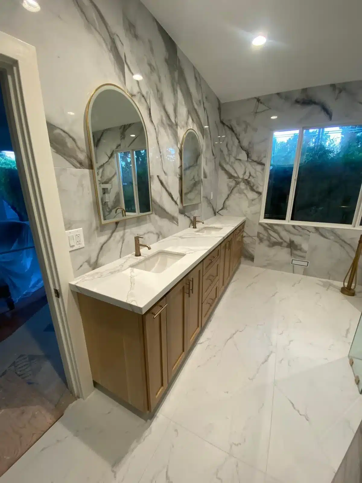 Bathroom with dual vanity, marble walls and floor, and two gold-framed mirrors